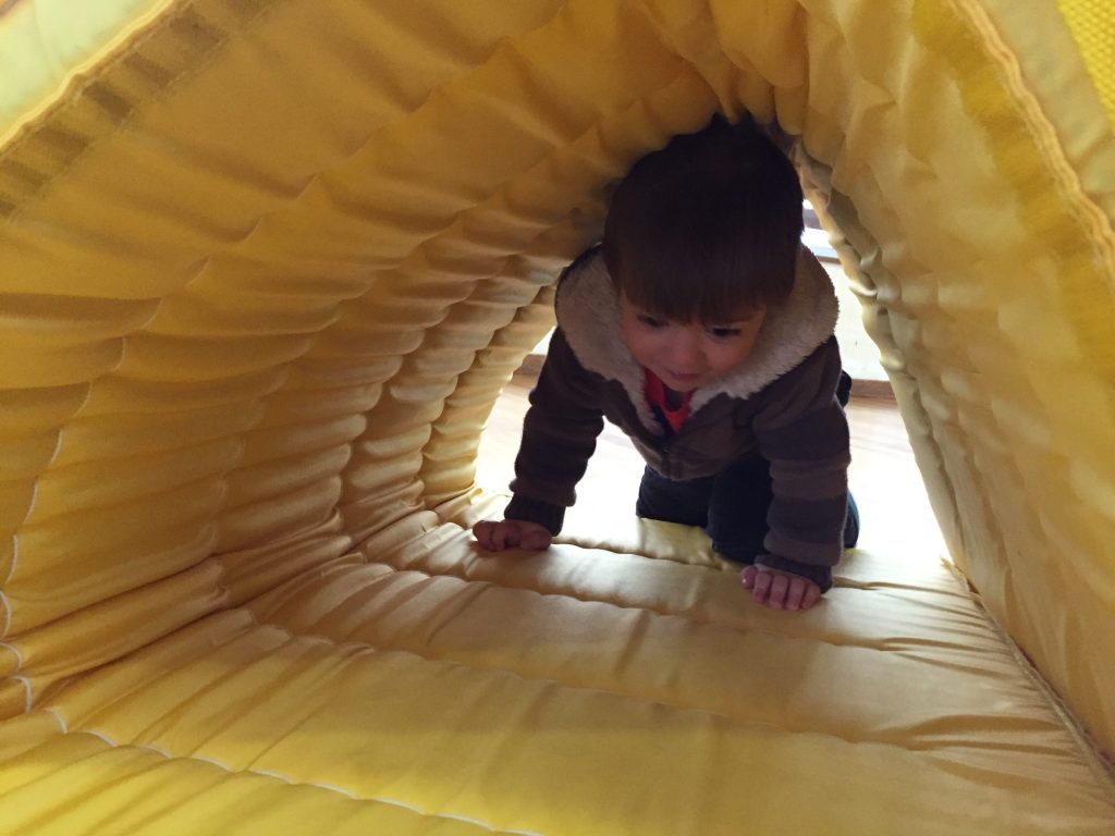 A young boy is crawling through a soft yellow tunnel.